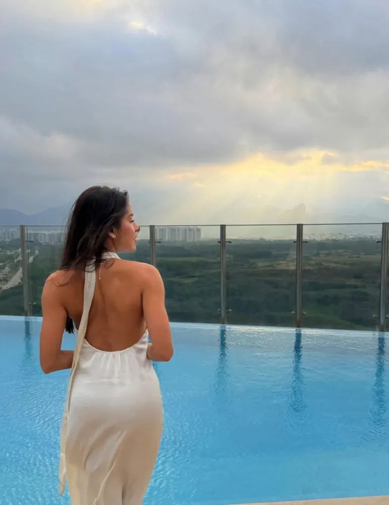 Ulhiana Rozeno seen from behind in a satin dress, by a pool overlooking Rio's mountains at dusk.